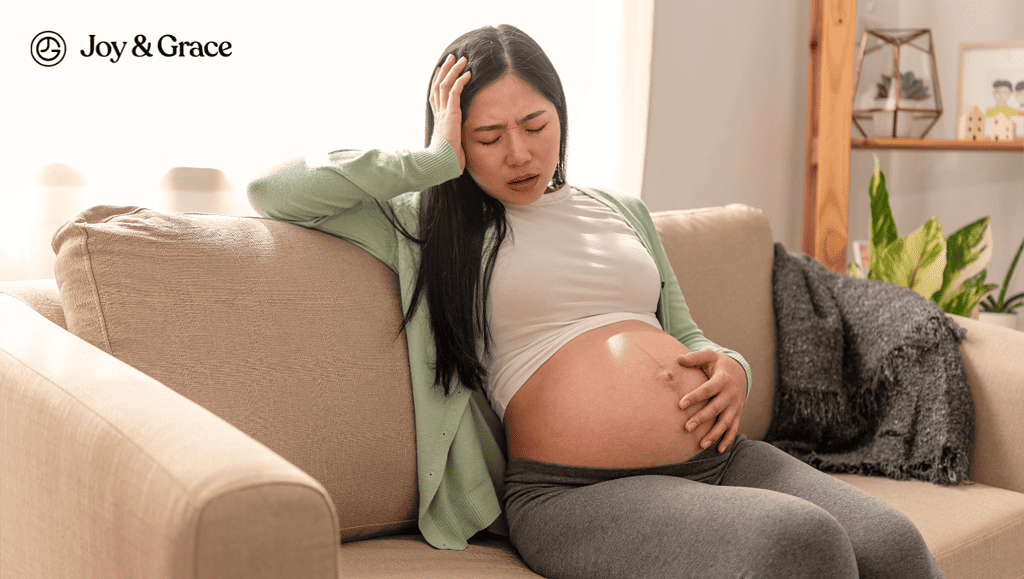 a pregnant woman sits on the couch with her arms behind her head