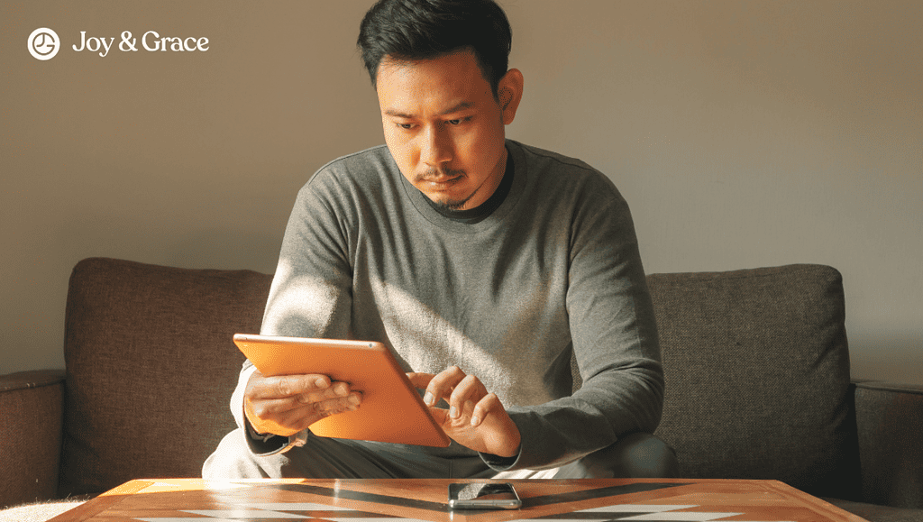 a man in a sweater holding a tablet and sitting down