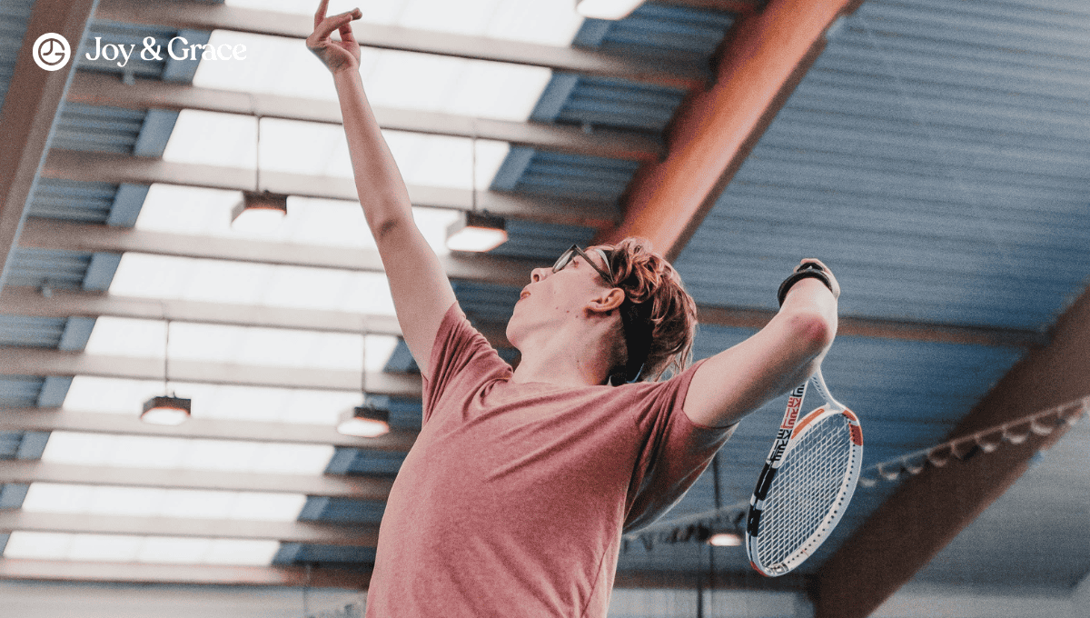 a man standing in an indoor gym holds a tennis racket and extends the arm