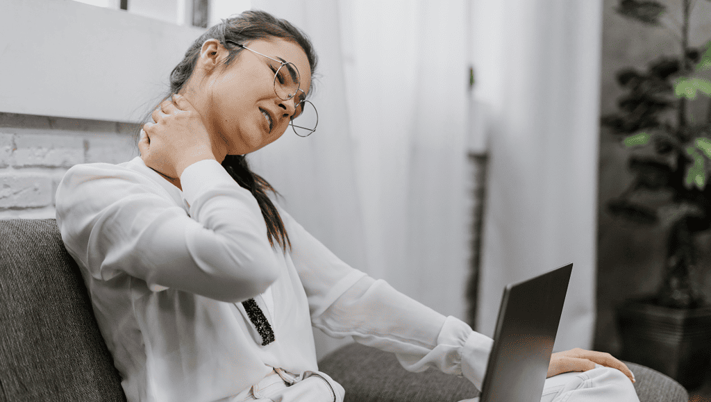 a woman sitting on the couch while touching her neck pain