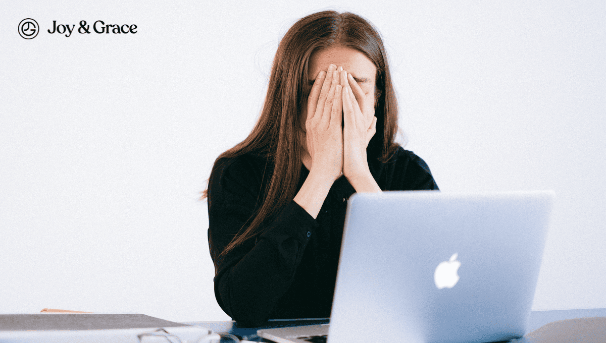 a woman is covering her face at a desk with a laptop