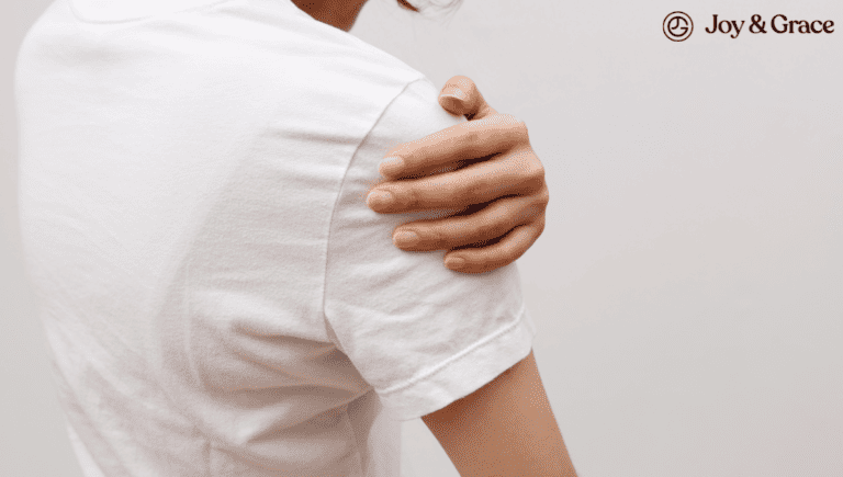 The back of a woman wearing a white t-shirt experiencing shoulder pain.