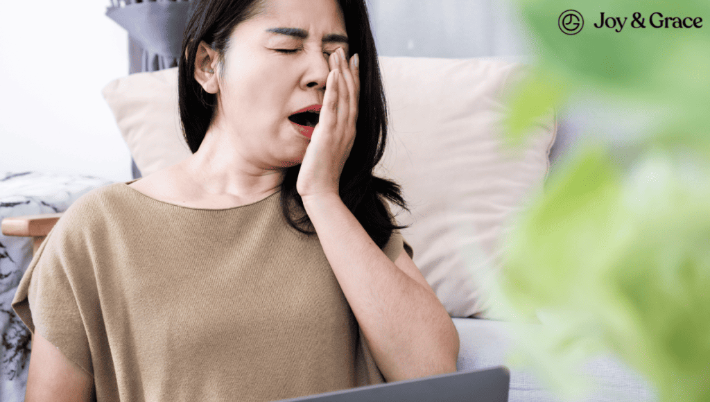 A woman sitting on a laptop, experiencing neck pain after yawning.