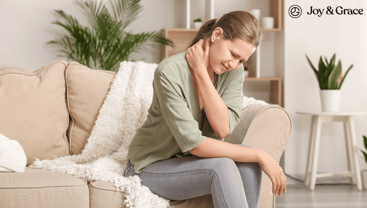 A woman sitting on a couch with her hand on her neck, seeking relief from neck pain.