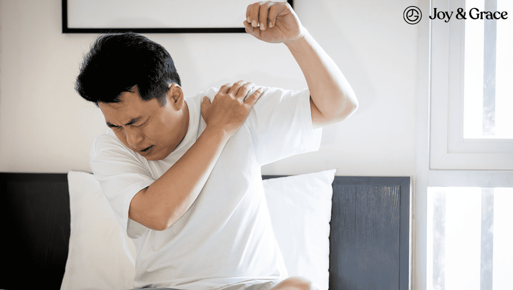 A man experiencing shoulder blade pain lays on a bed with his arms raised.