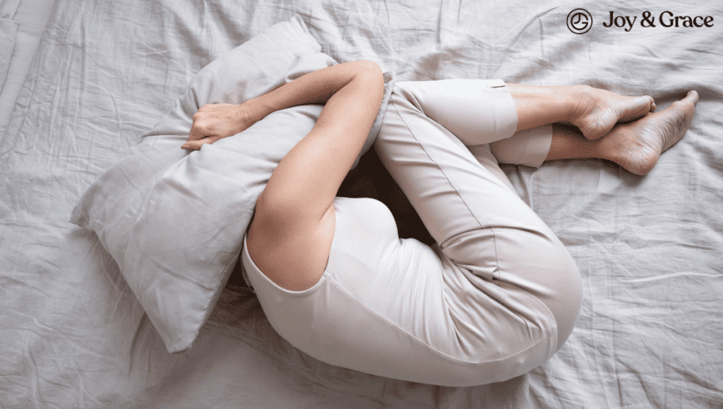 A woman experiencing neck pain lays on a bed with a pillow under her head.