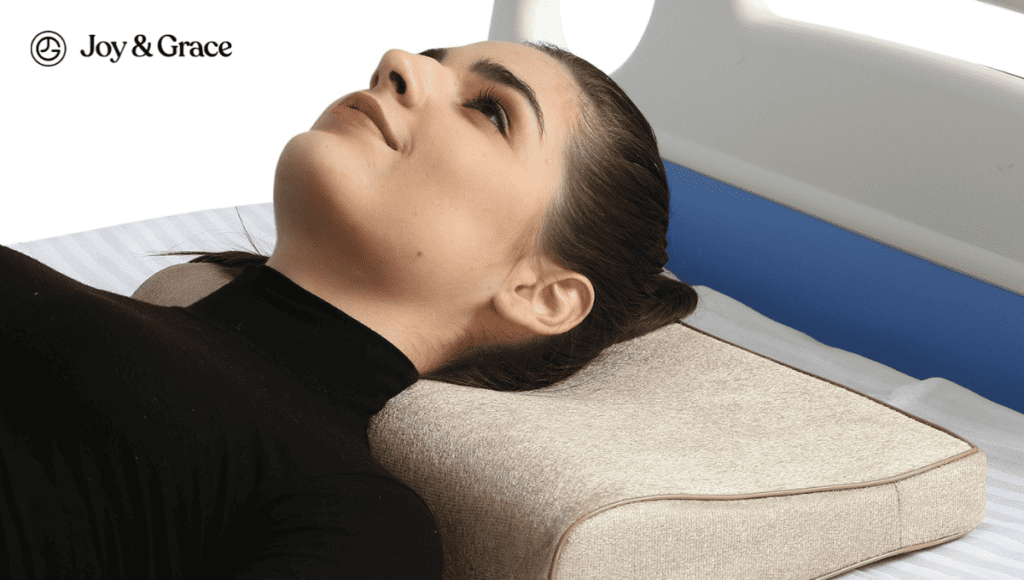 A woman experiencing neck pain on a bed, adjusting her sleeping position with the help of a pillow.