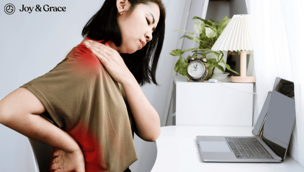 A woman is sitting in front of a laptop with a pain in her shoulder and back.