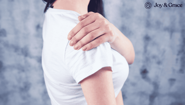 A woman is holding her shoulder in front of a gray background, displaying visible signs of shoulder pain.