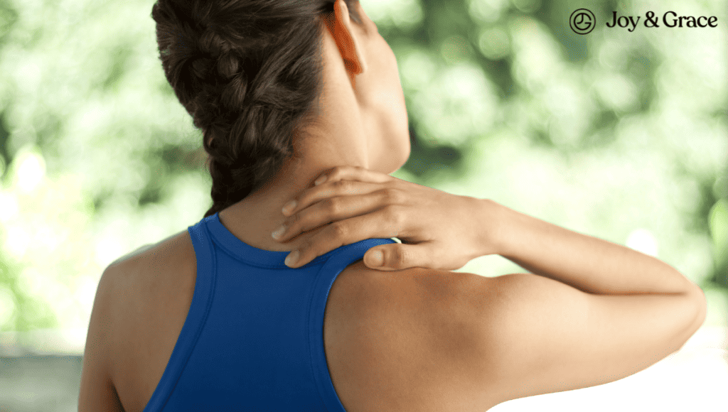 A woman in a blue shirt is grimacing as she holds her neck, possibly experiencing shoulder or trapezius pain.