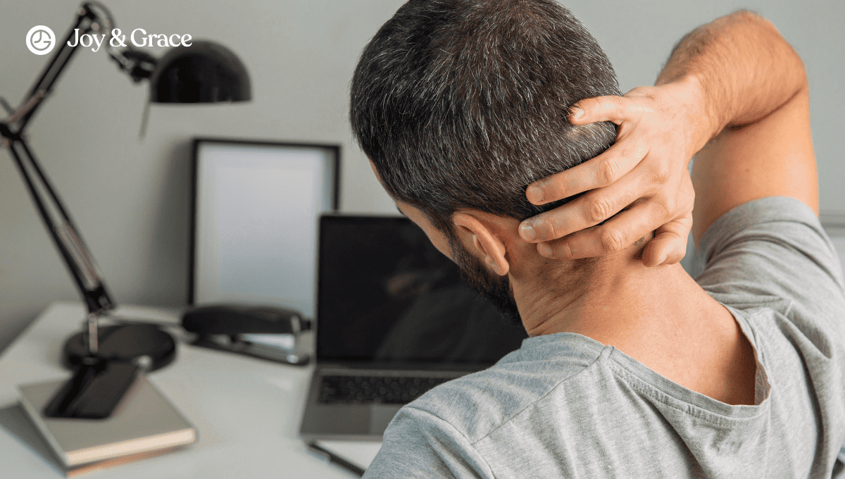 A man is sitting at his desk experiencing neck pain from prolonged computer use.