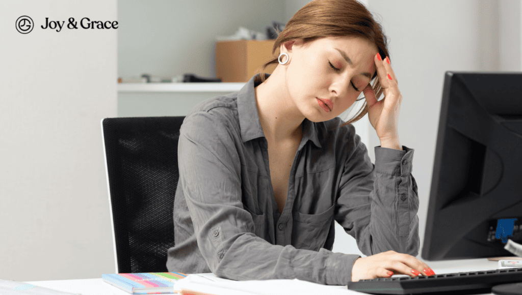 A woman is sitting at a desk with her head in her hands, massaging her neck.