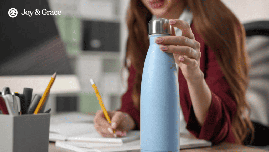 A woman is sitting at her desk experiencing neck pain that radiates to her shoulder. She holds a blue water bottle in an attempt to alleviate the myofascial pain she is feeling.