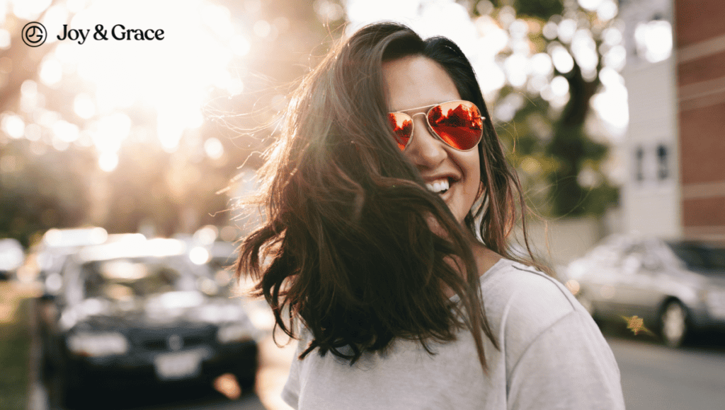 A woman wearing sunglasses and smiling in the street, providing the ultimate guide for neck and shoulder myofascial pain.