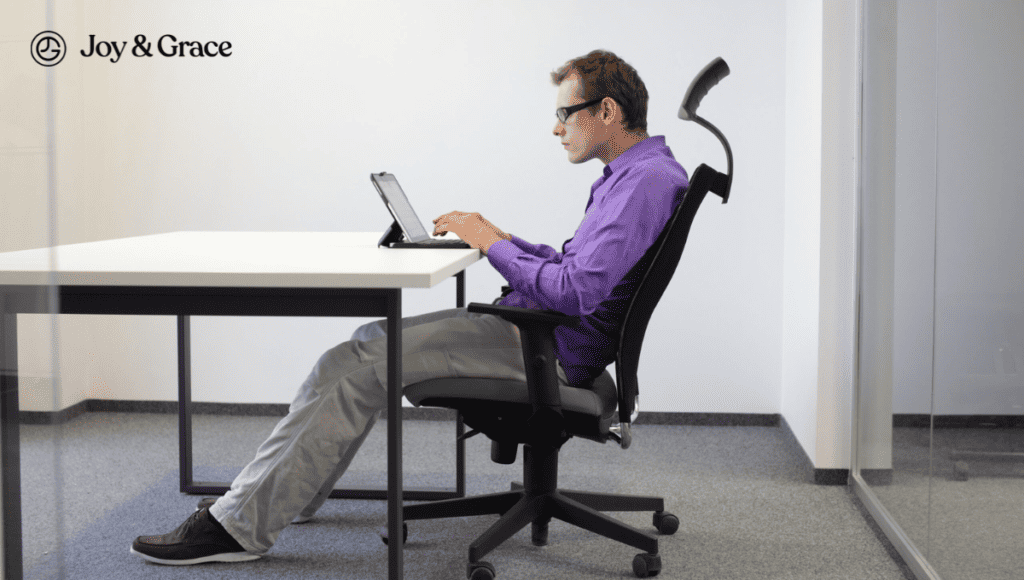 A man sitting in an office chair using a laptop, experiencing neck pain.