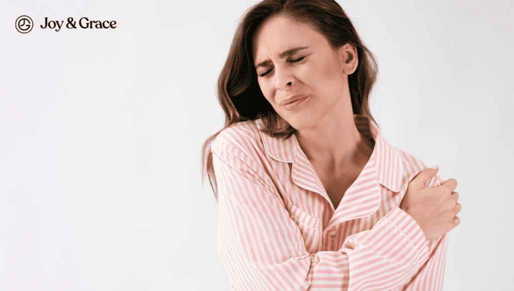 A woman in a pink shirt is holding her shoulder, seemingly experiencing shoulder pain.